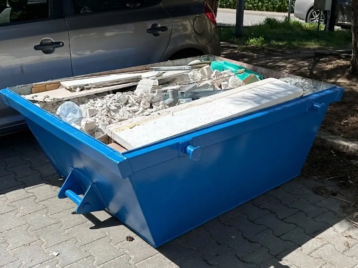 Niebieski kontener na odpady podstawiony na kostce brukowej przy bloku