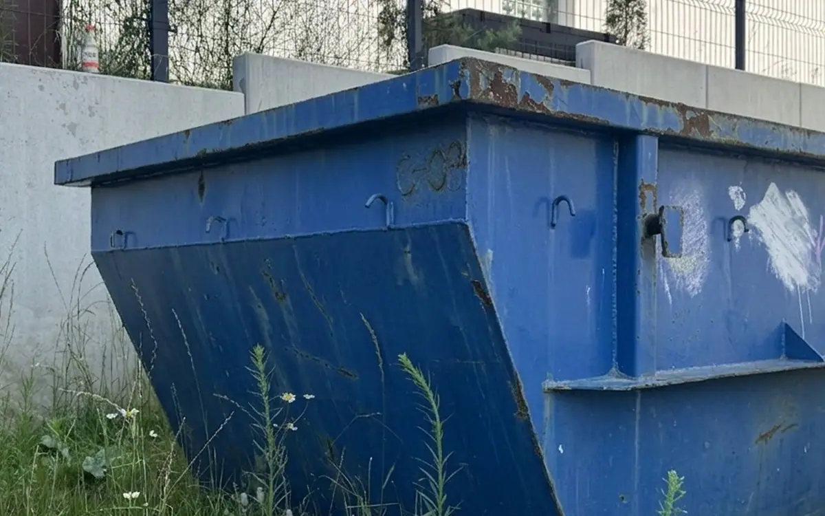 Pusty kontener na odpady odstawiony przy ogrodzeniu posesji