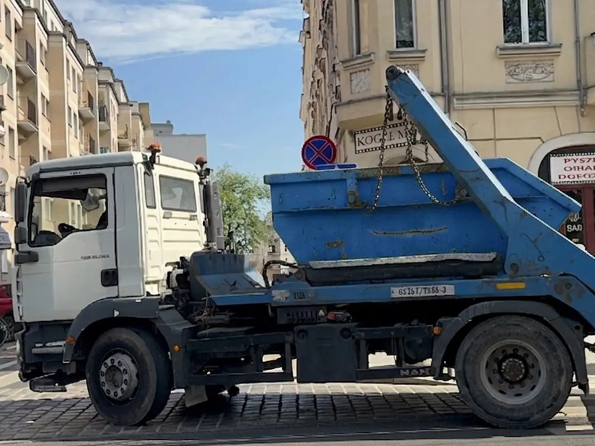 Samochód bramowy z kontenerem podstawiony przy kamienicy w mieście